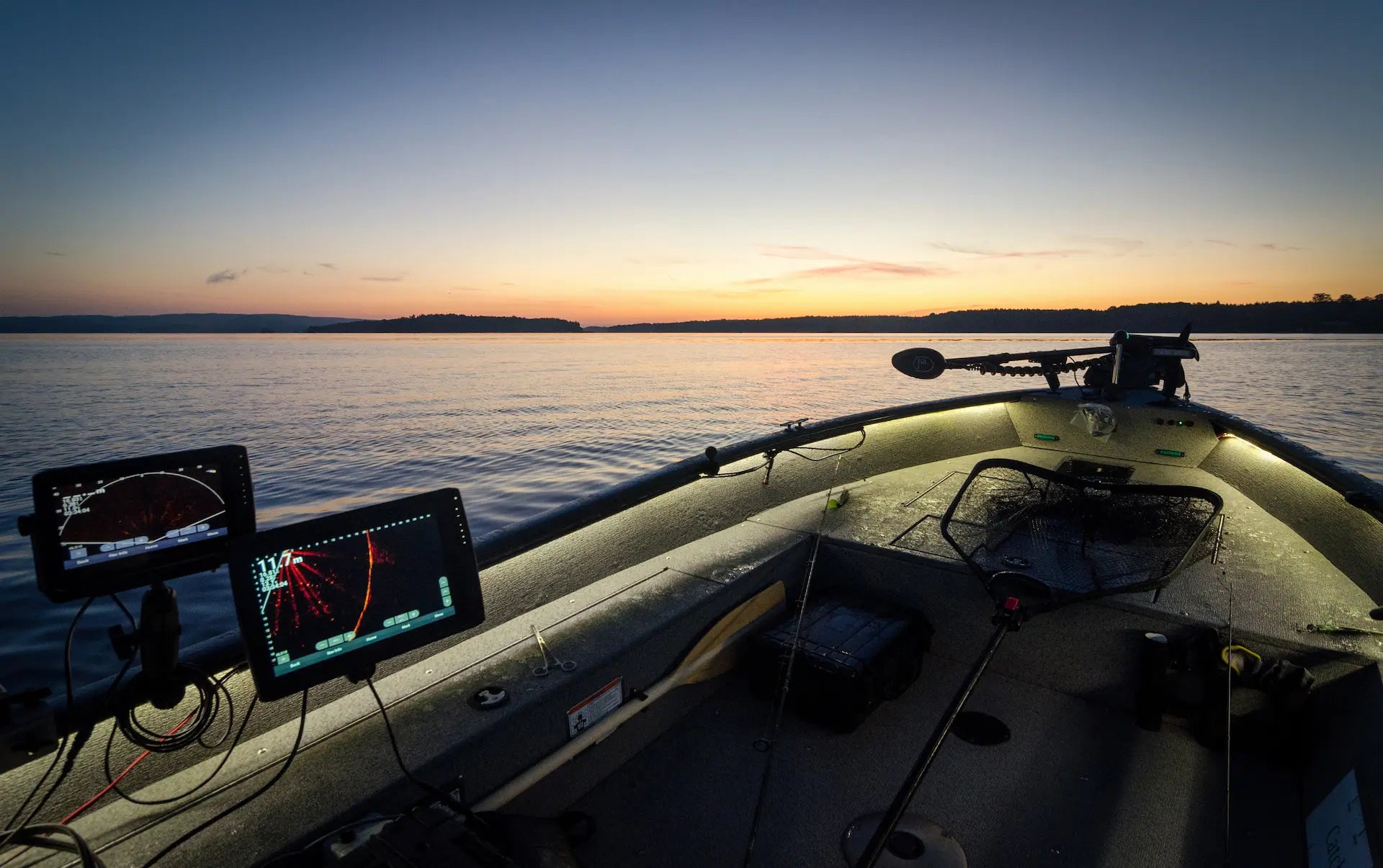 Fish finder and chartplotter displays on a bass boat at sunrise on a calm lake